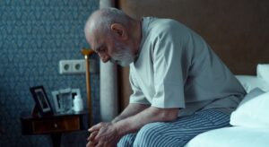older man sitting on the edge of a bed