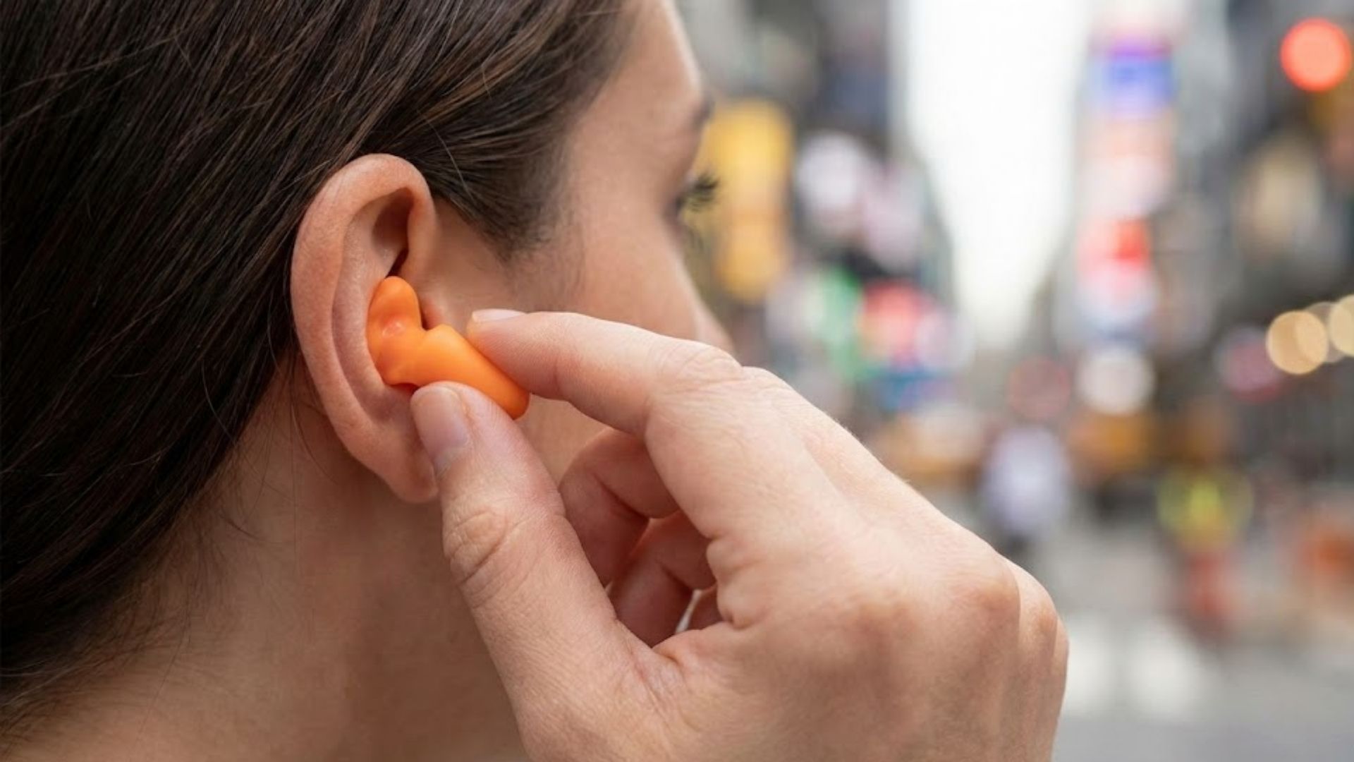 Close-up of a woman inserting an orange foam earplug.
